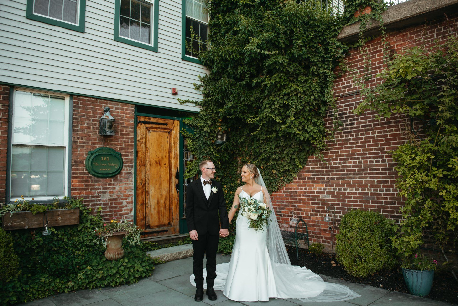 Bride and groom posing outside a brick house with ivy and wooden door