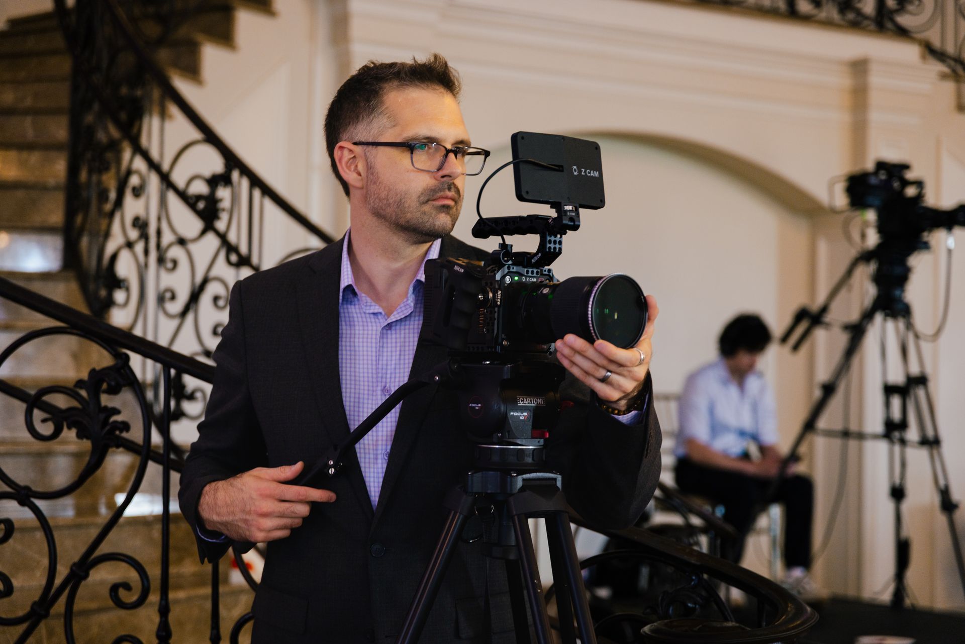 Man filming with a camera rig on a staircase, with another cameraman blurred in the background