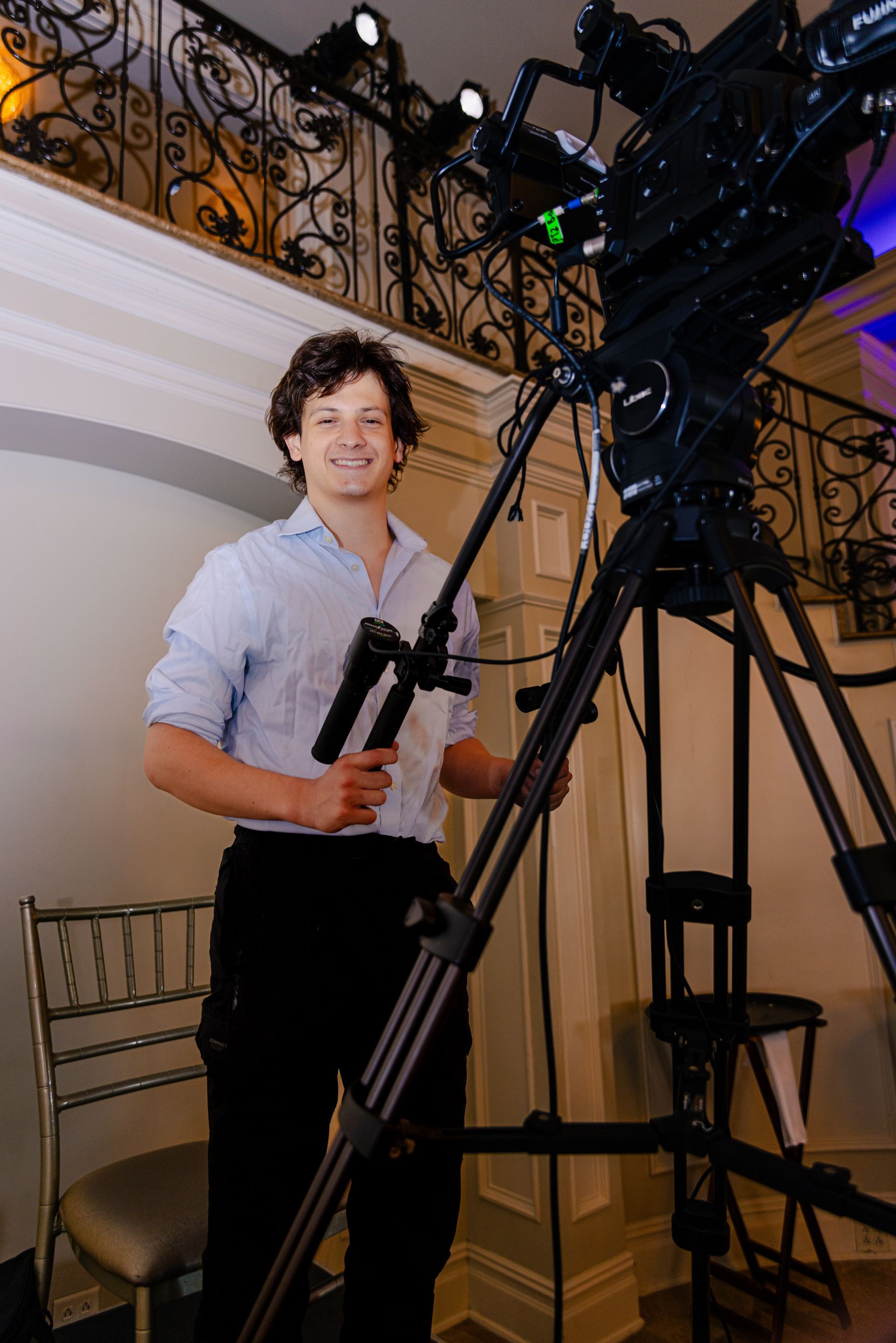 Person operating a large professional camera rig on a tripod indoors at an event venue