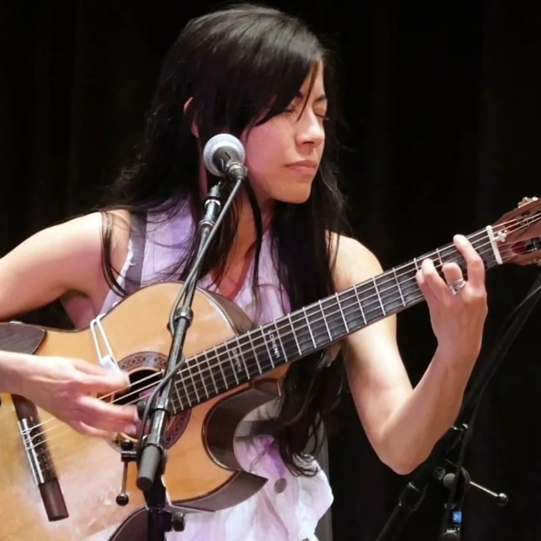 Musician playing acoustic guitar and singing into a microphone onstage