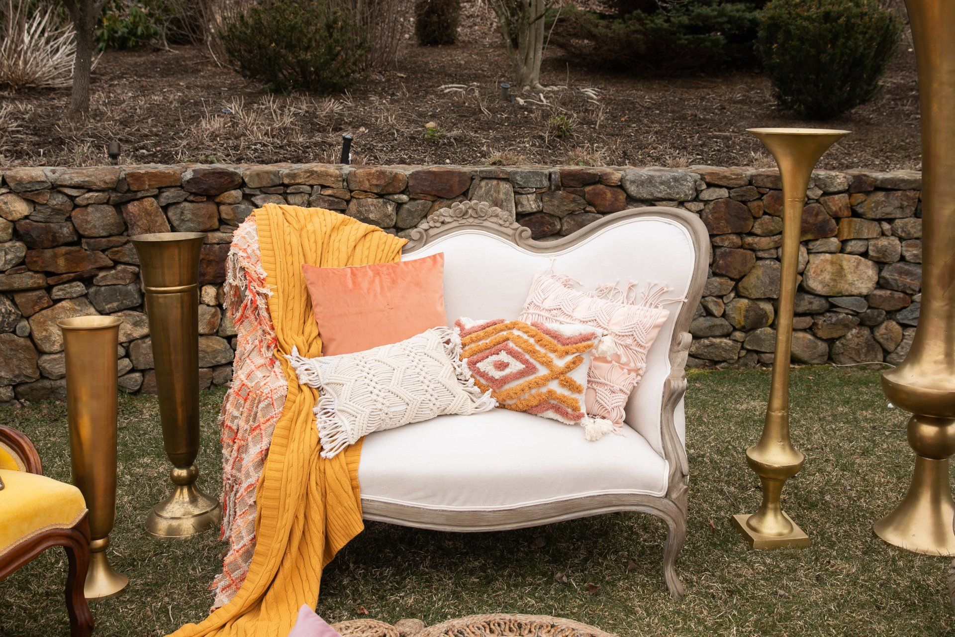 White tufted loveseat with patterned pillows and mustard throw in a rustic outdoor garden setting