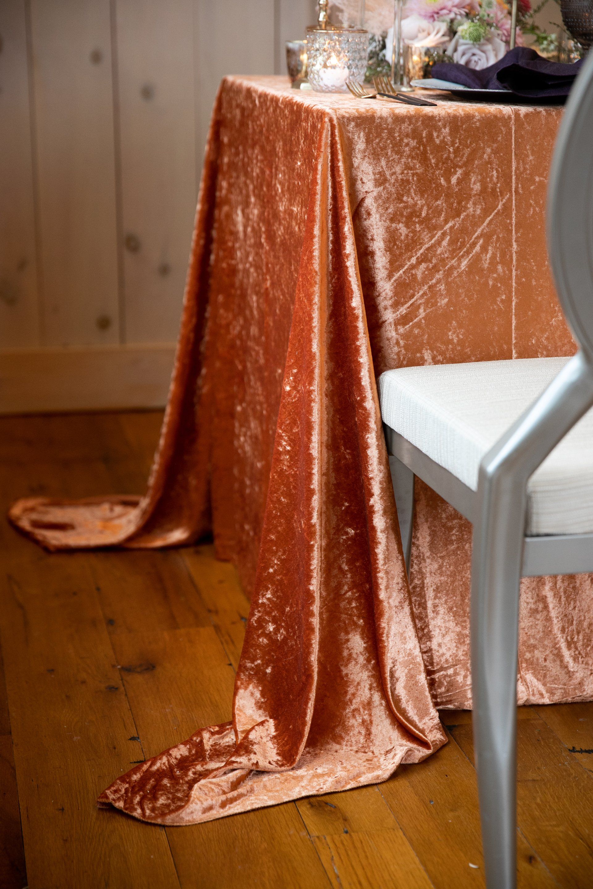 Copper sequin tablecloth draped over a table beside a white chair in a wood-paneled room