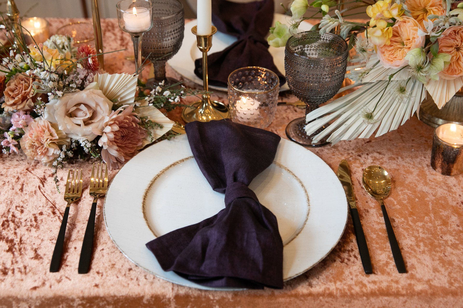 Elegant table setting with rose-gold decor, white plates, dark napkins, and floral arrangements