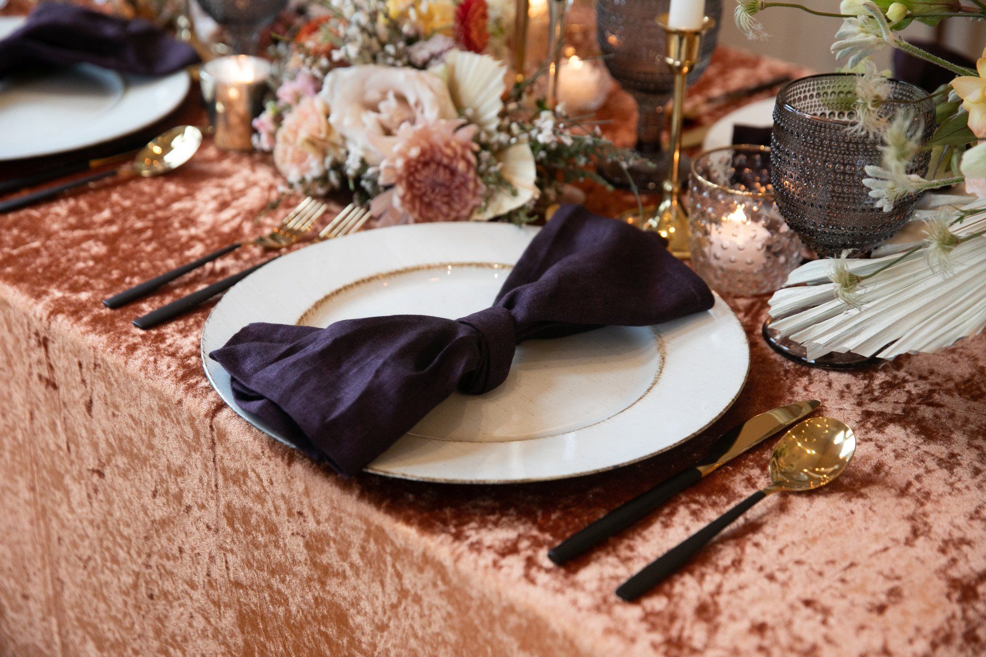 Elegant pink table setting with black napkins, white plates, gold flatware, and floral decor