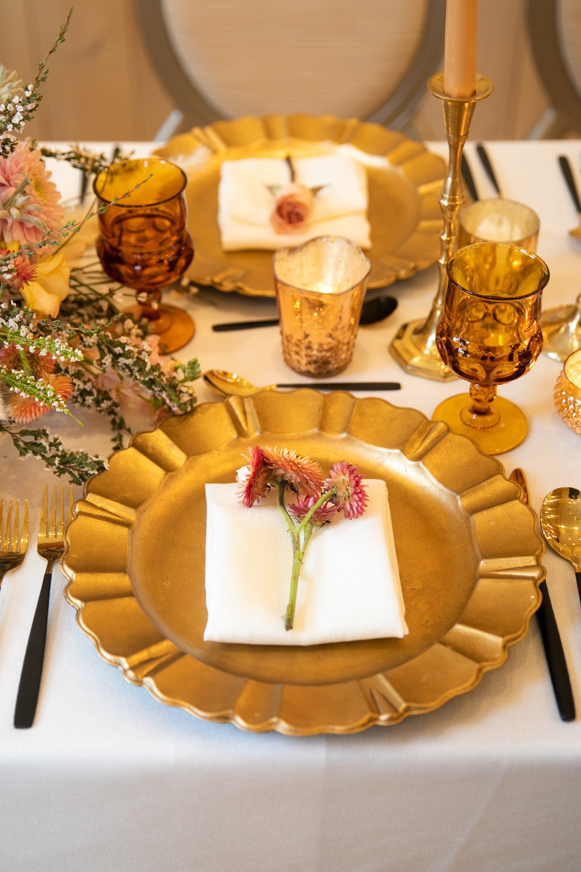 Elegant dining table with gold chargers, white napkins, and amber glassware, set for a formal meal