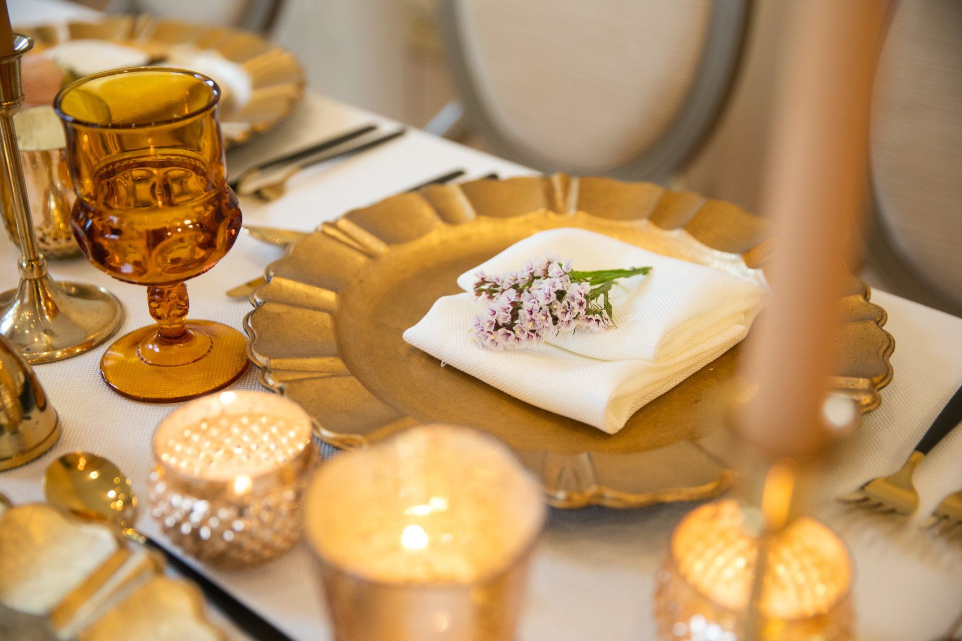 Elegant table setting with gold candleholders, folded napkins, and decorative plates on a white tablecloth