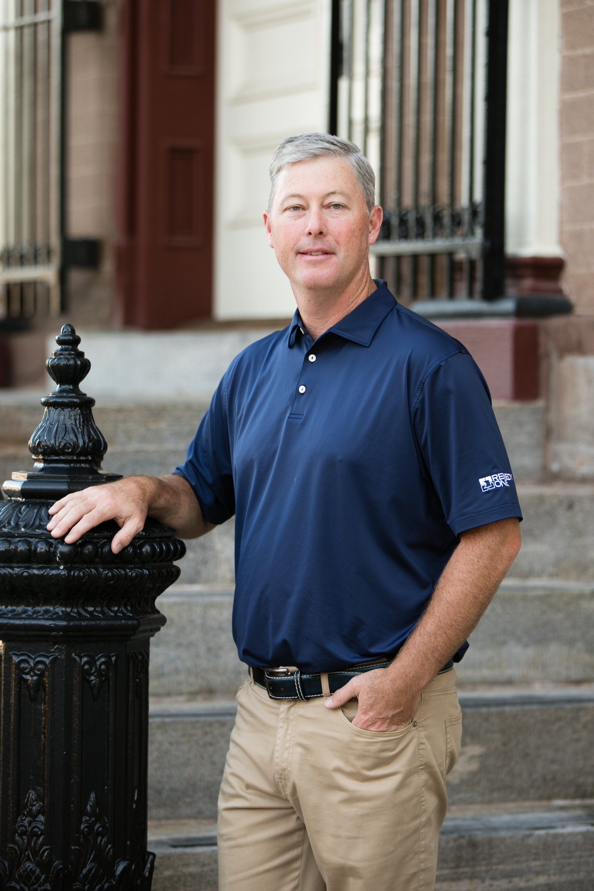 Man in navy polo and khaki pants standing by a black railing on stone steps outside a building