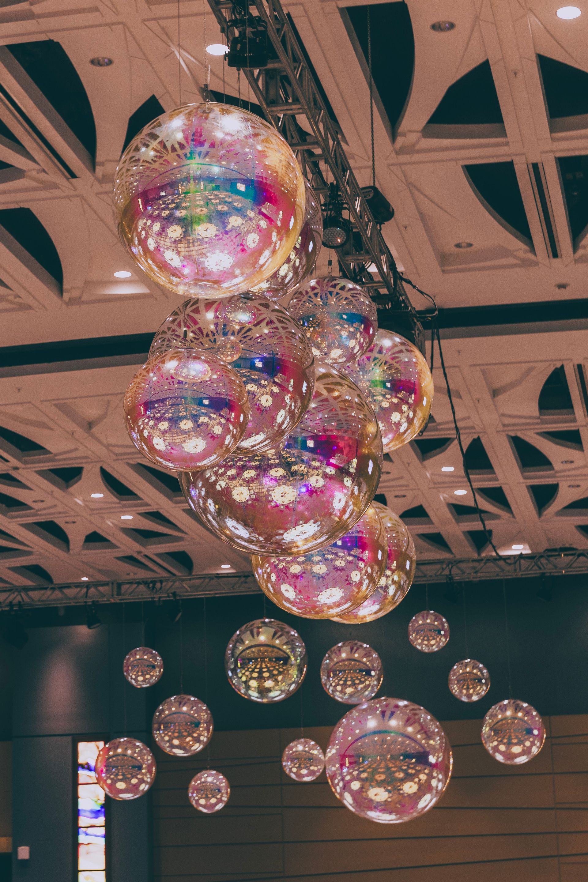 Cluster of colorful hanging glass spheres under a geometric ceiling in a modern indoor space