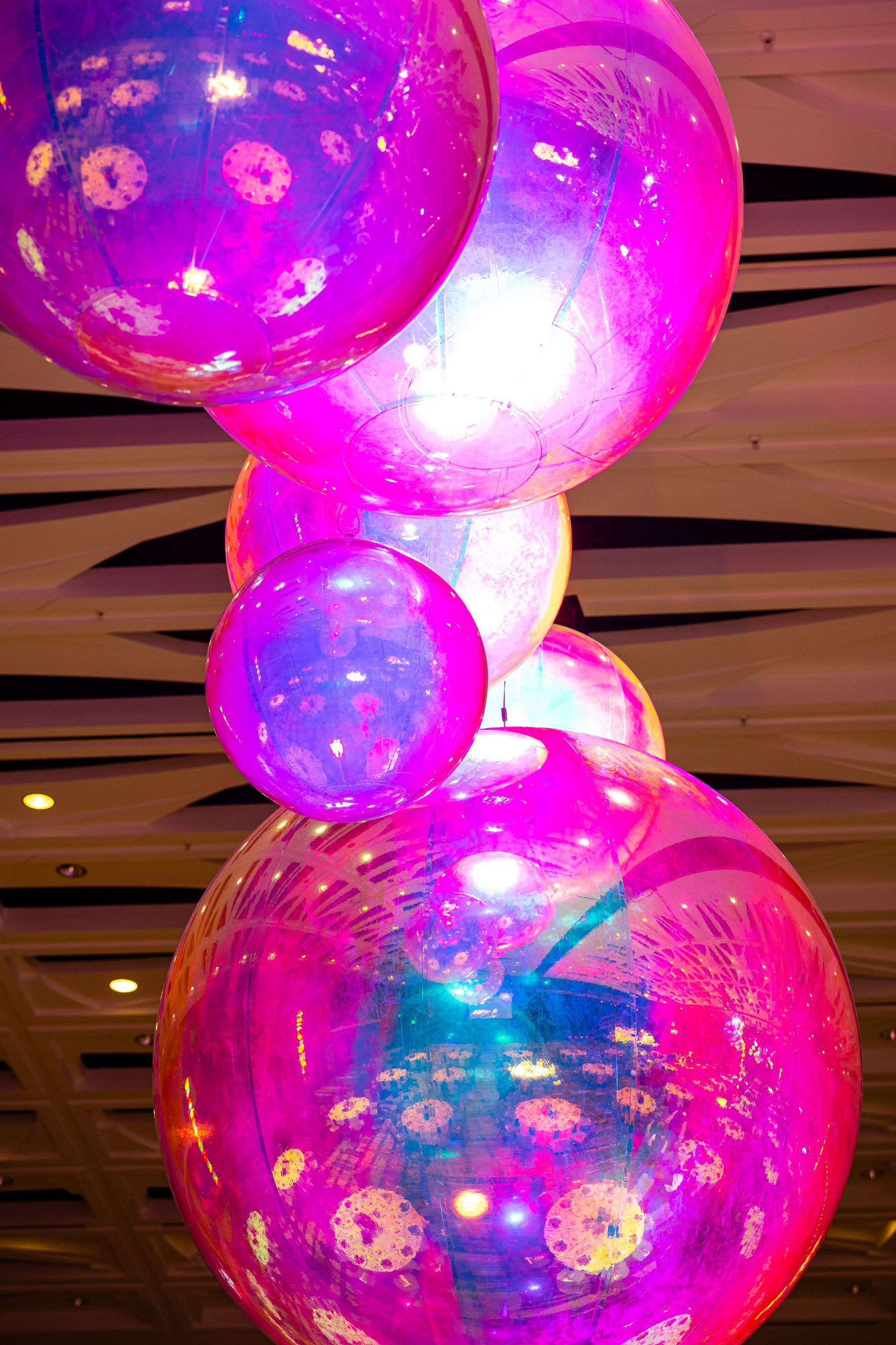 Glowing pink and purple translucent balloons or spheres stacked vertically indoors