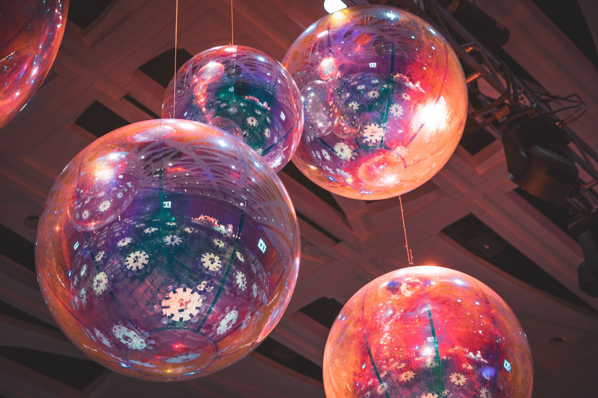 Colorful illuminated glass orbs hanging indoors, reflecting pink, purple, and blue light.