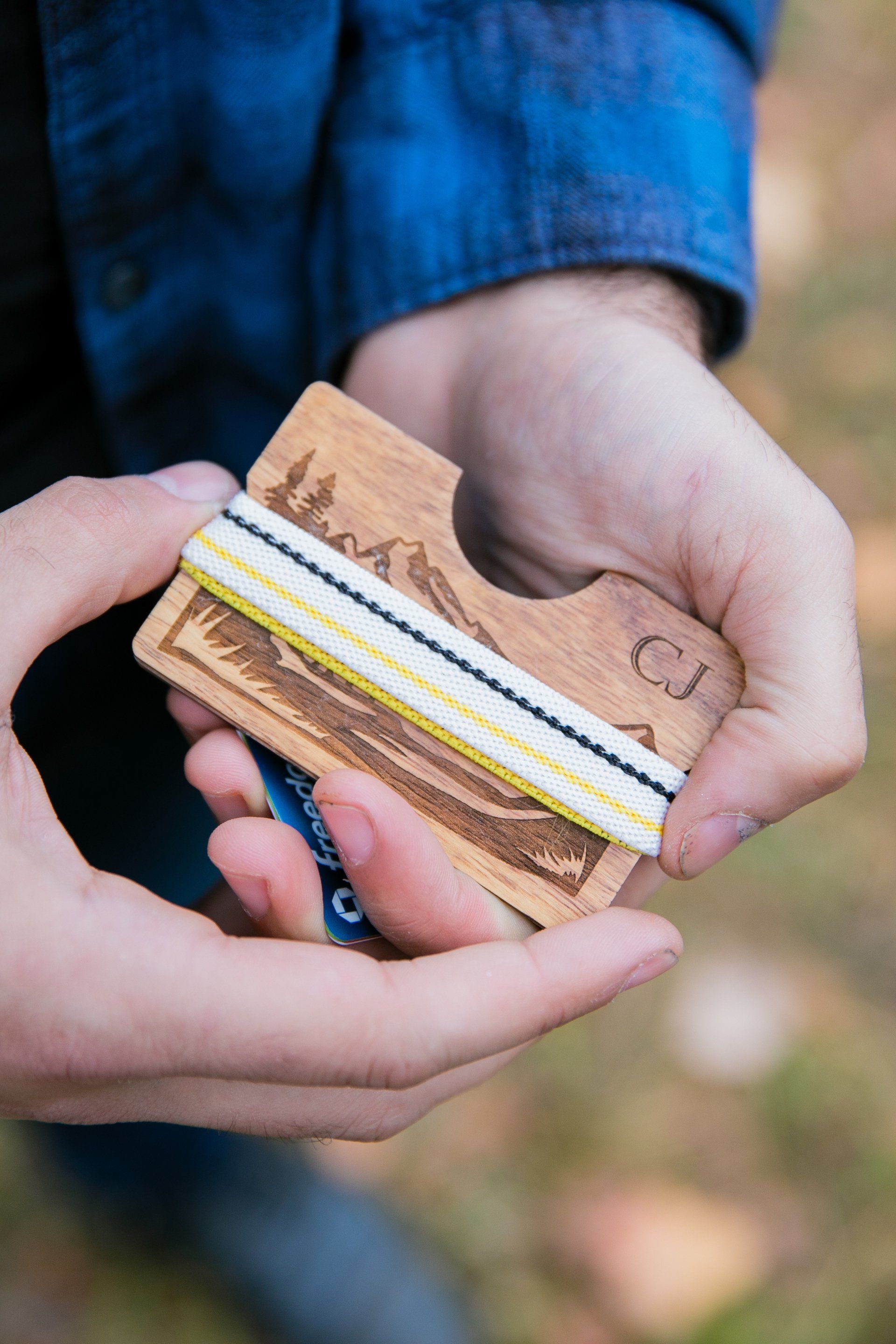 Hands holding a small cardboard piece with layered colored strips, outdoors on a blurred background.