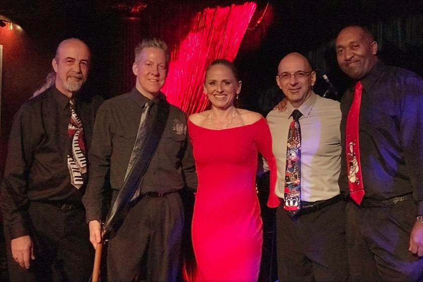 Five people posing together indoors, dressed in formal attire, with the woman in a bright pink dress.