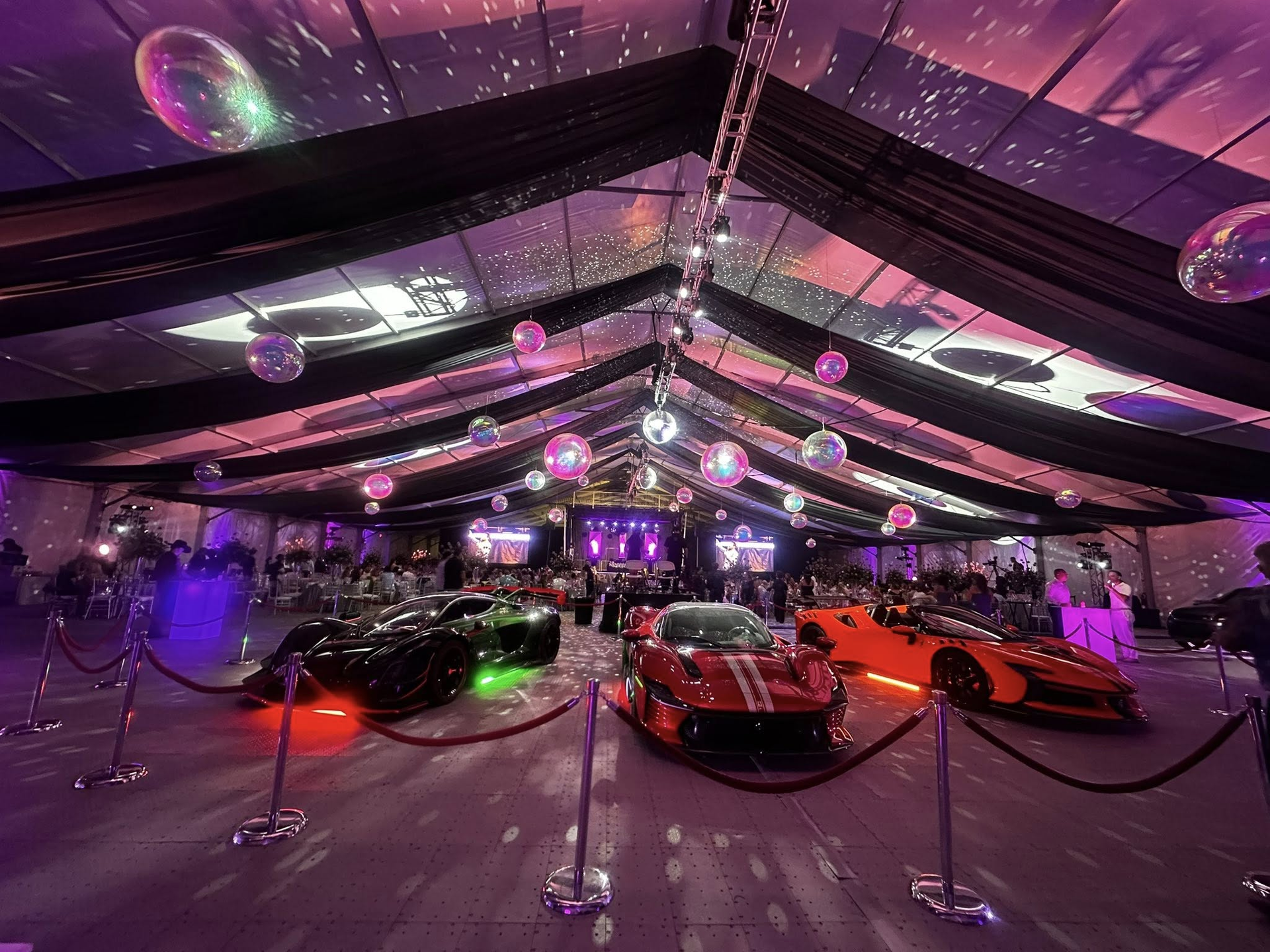 Tent display with colorful sports cars, neon lights, and reflective ceiling at an indoor event