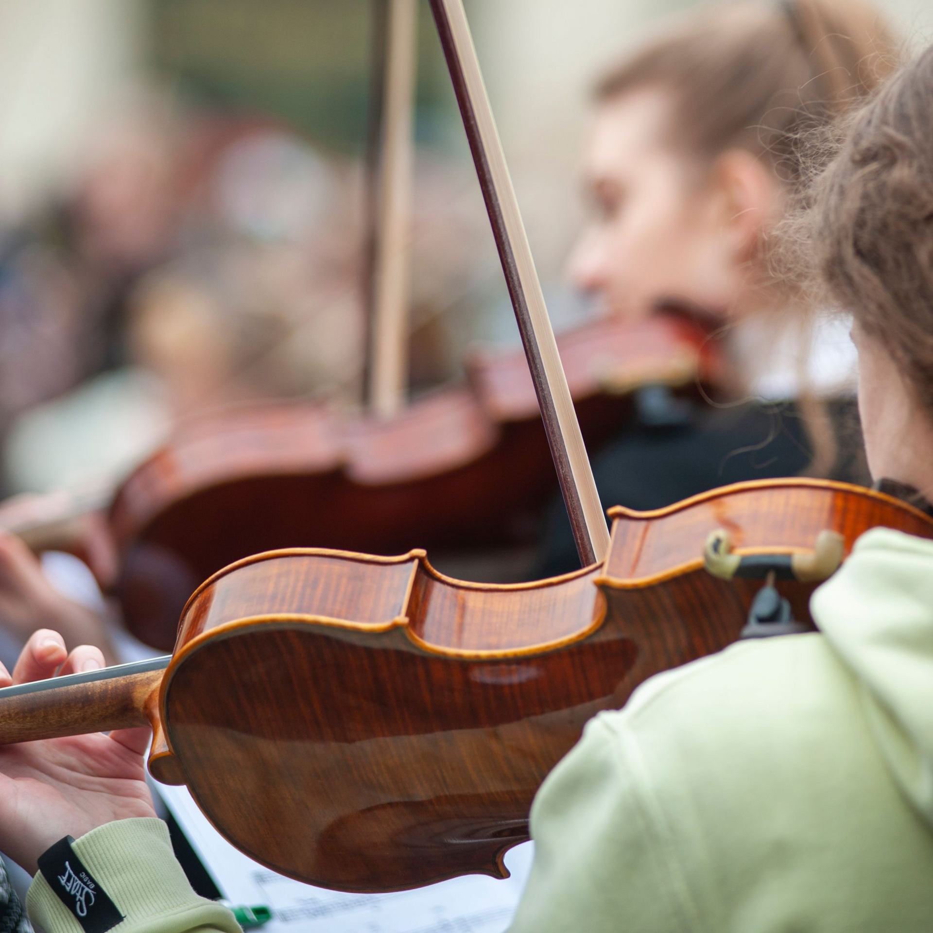 Close-up of a violin being played in an orchestra rehearsal, with blurred musicians in the background