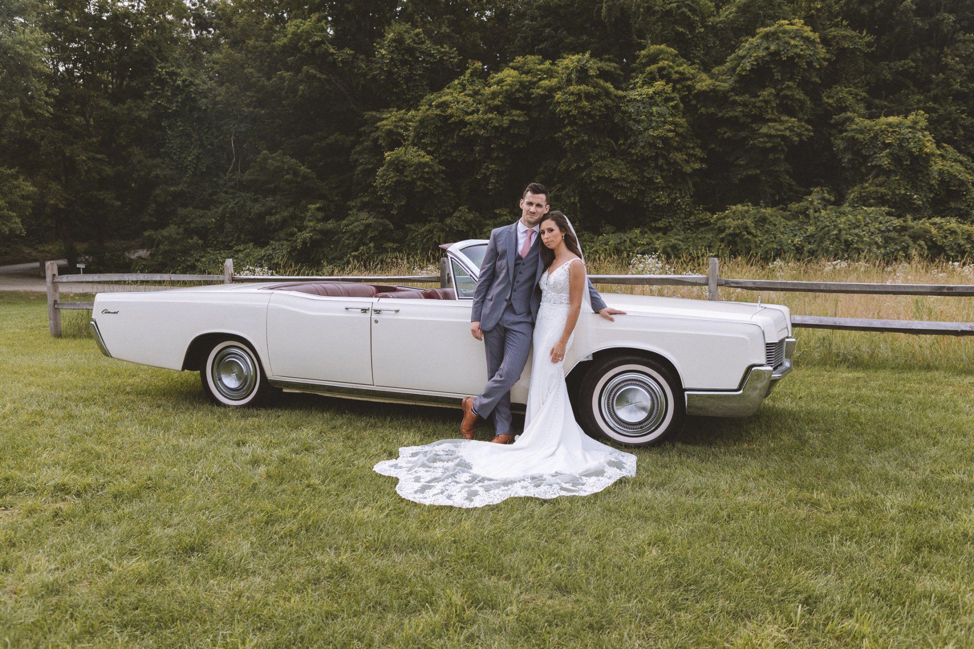 Bride and groom posing beside a white vintage convertible in a grassy field