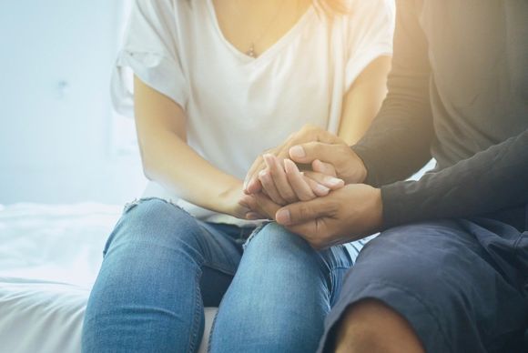 Un uomo e una donna si tengono per mano mentre sono seduti su un letto.