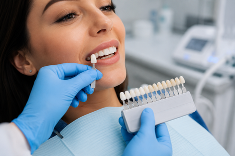 In una clinica, un dentista abbina la tonalità di un dente a quella di un paziente sorridente utilizzando una scala cromatica.