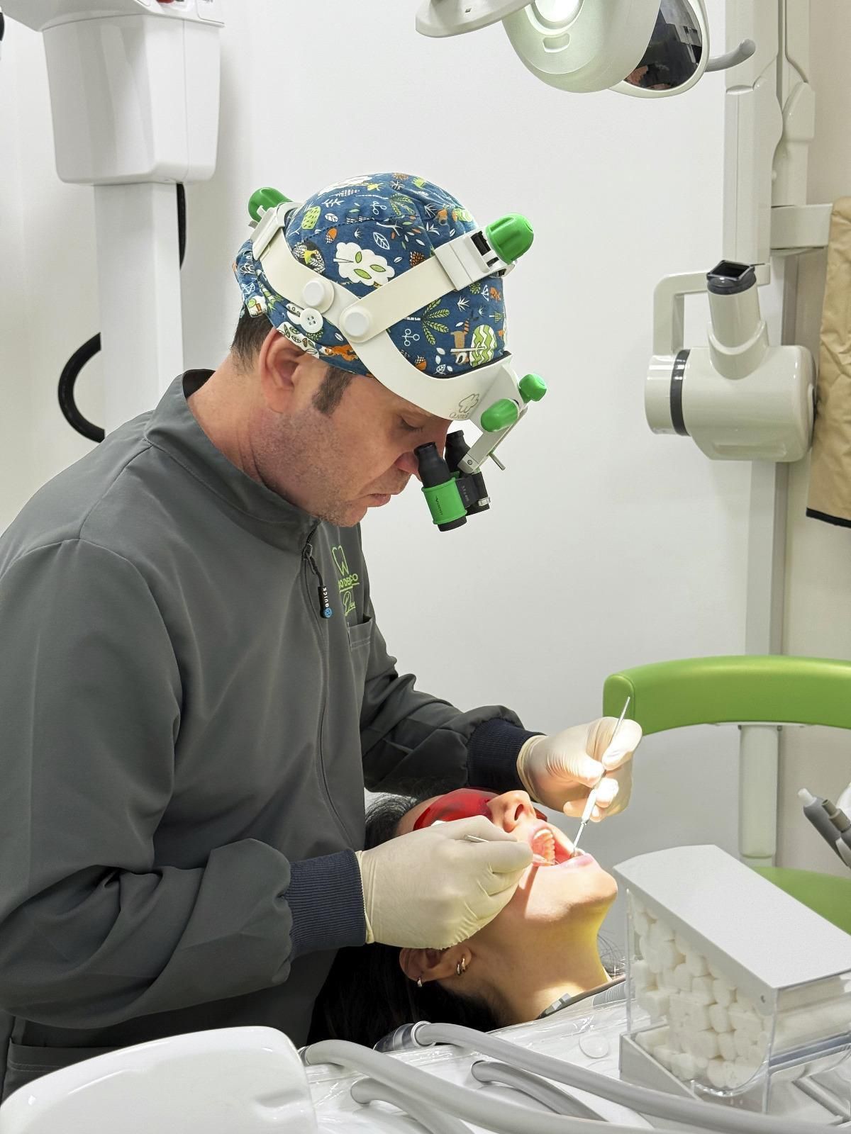 Un dentista con indosso una lente d'ingrandimento esamina la bocca di un paziente in una sala operatoria.