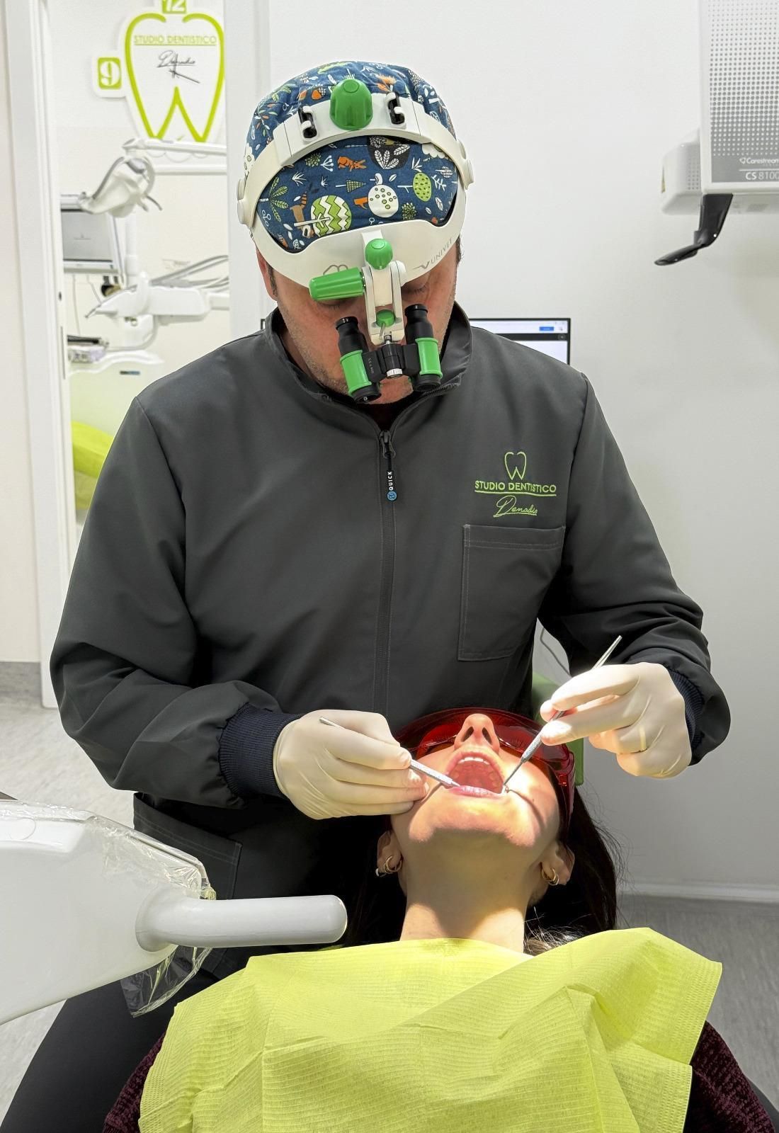 Un dentista visita un paziente seduto sulla poltrona odontoiatrica, indossando guanti e utilizzando strumenti dentali in una clinica.
