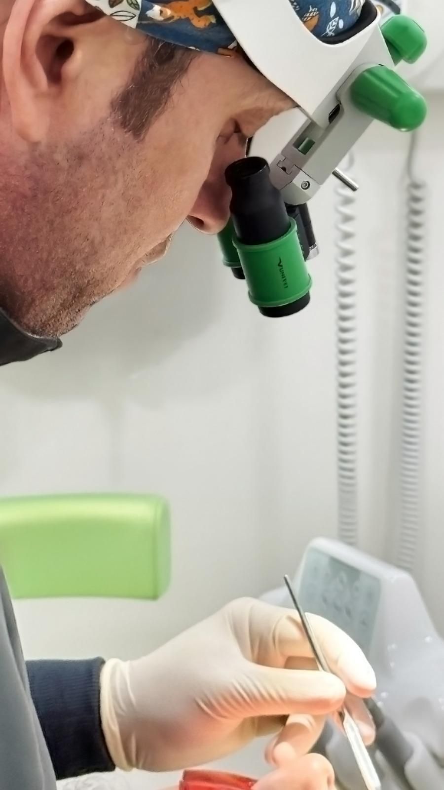 Un dentista con indosso una lente d'ingrandimento esegue una procedura odontoiatrica con le mani guantate e uno strumento.
