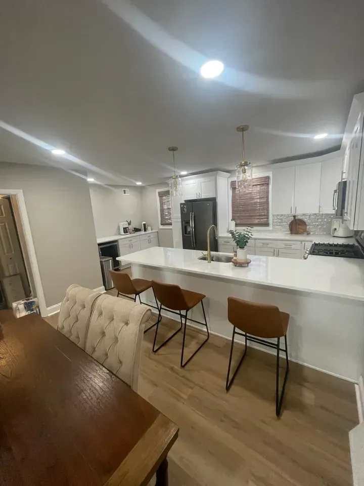 Modern kitchen with white countertops, brown bar stools, and wooden dining table.