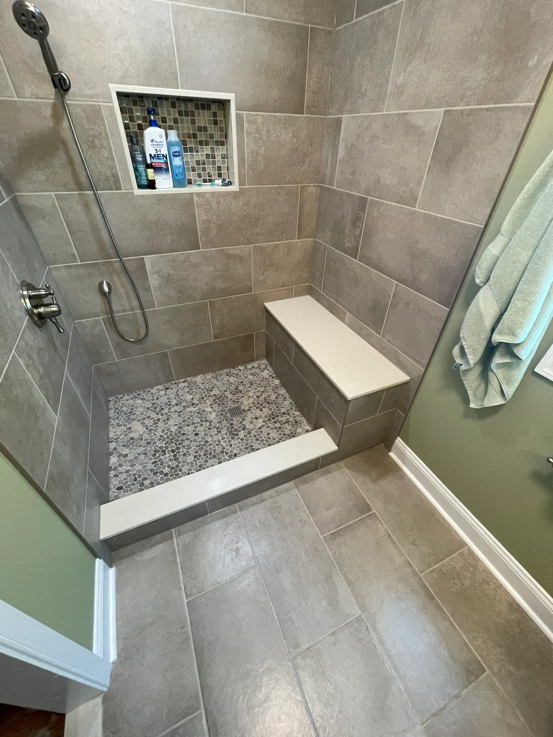 Shower stall with gray tile, pebble floor, built-in bench, and shampoo niche.