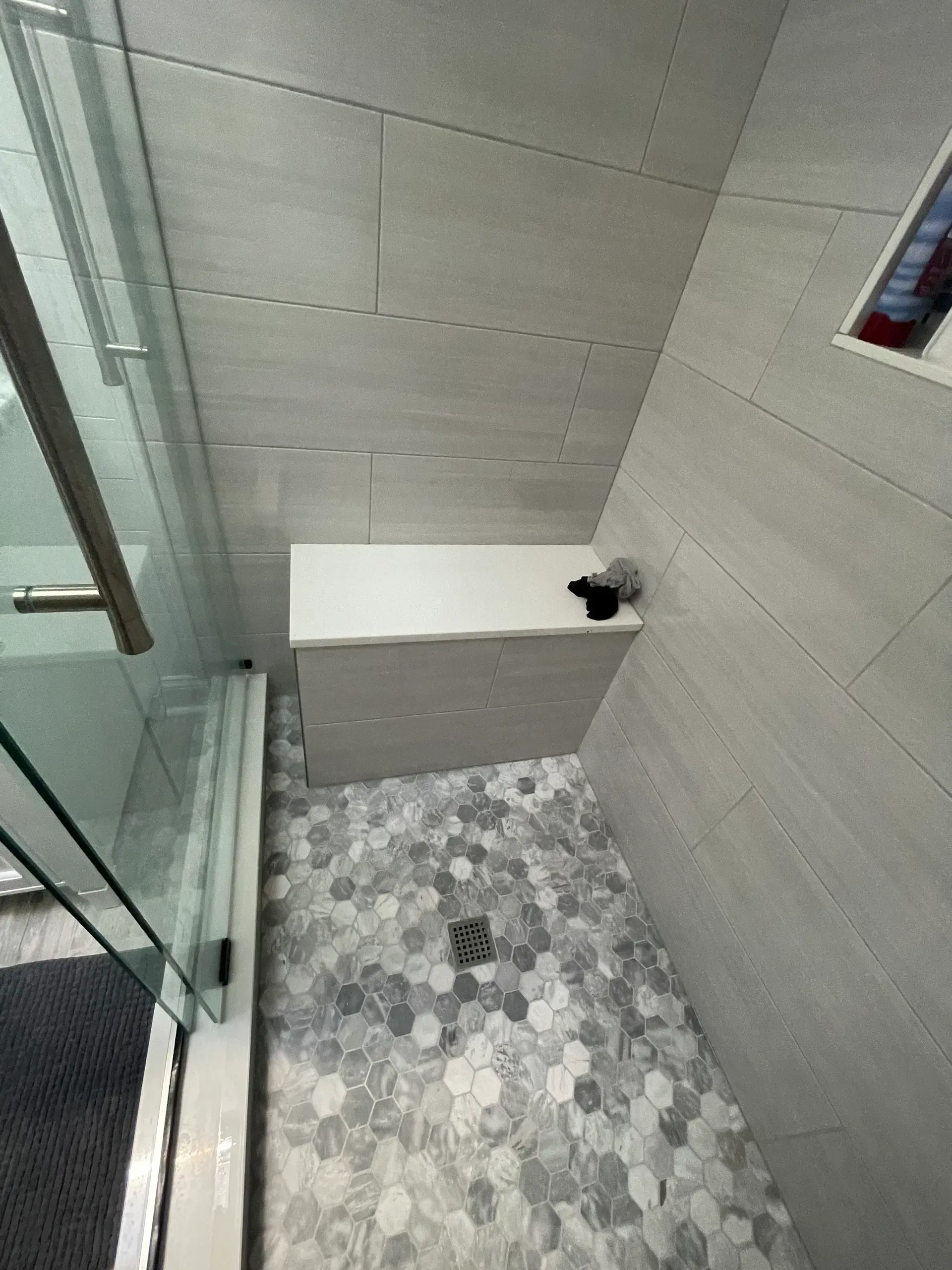 Shower with gray tiled walls, a white bench, and a hexagonal tile floor. 