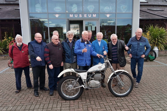 A group of men standing next to a motorcycle in front of a museum