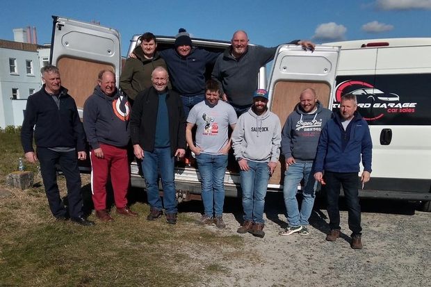 A group of men standing in front of a white van with the word garage on the side