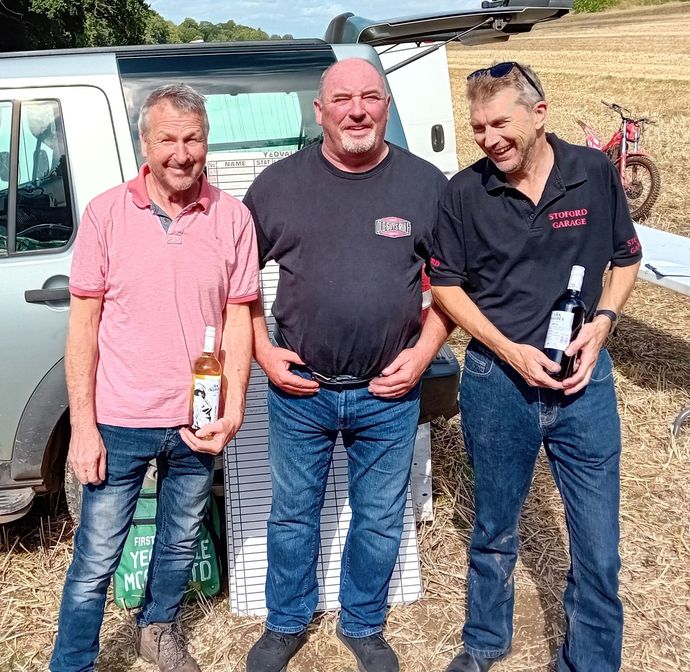 Three men standing next to each other holding bottles of wine