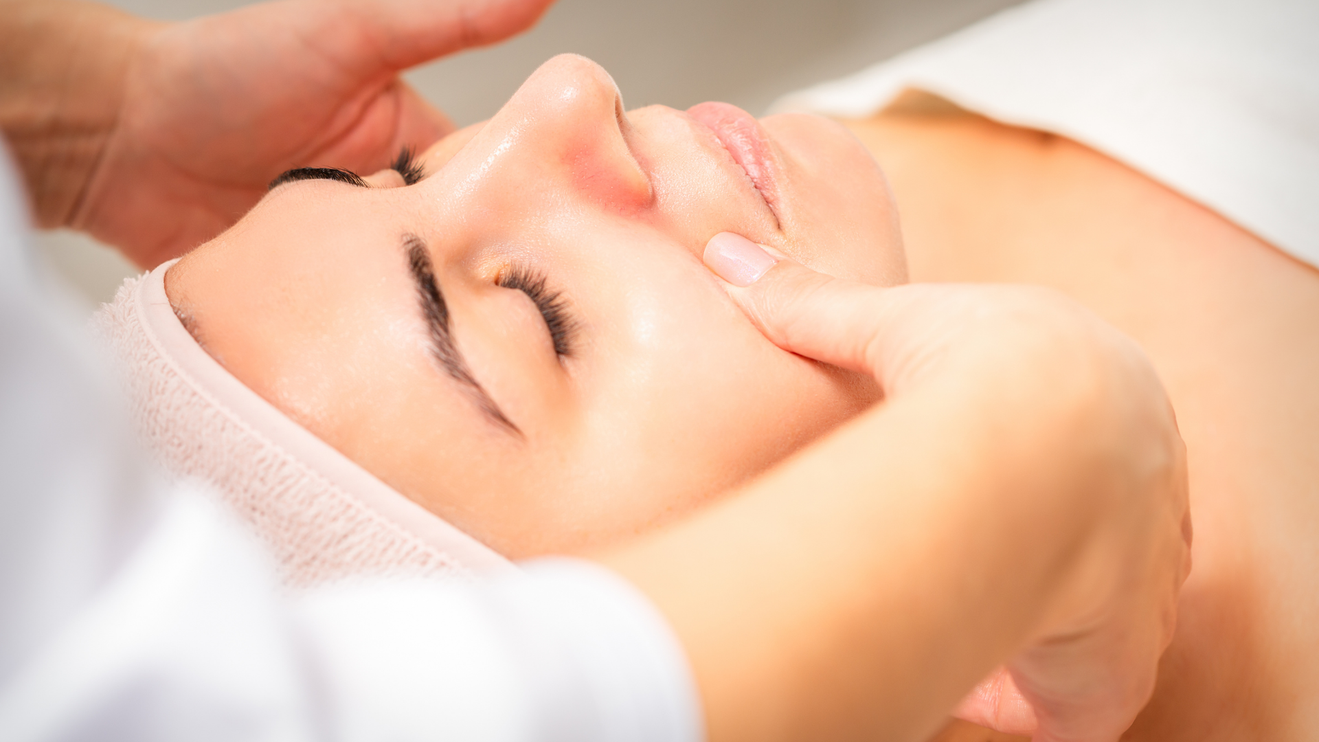 A person receiving a shoulder massage while lying on a white towel, eyes closed, smiling.