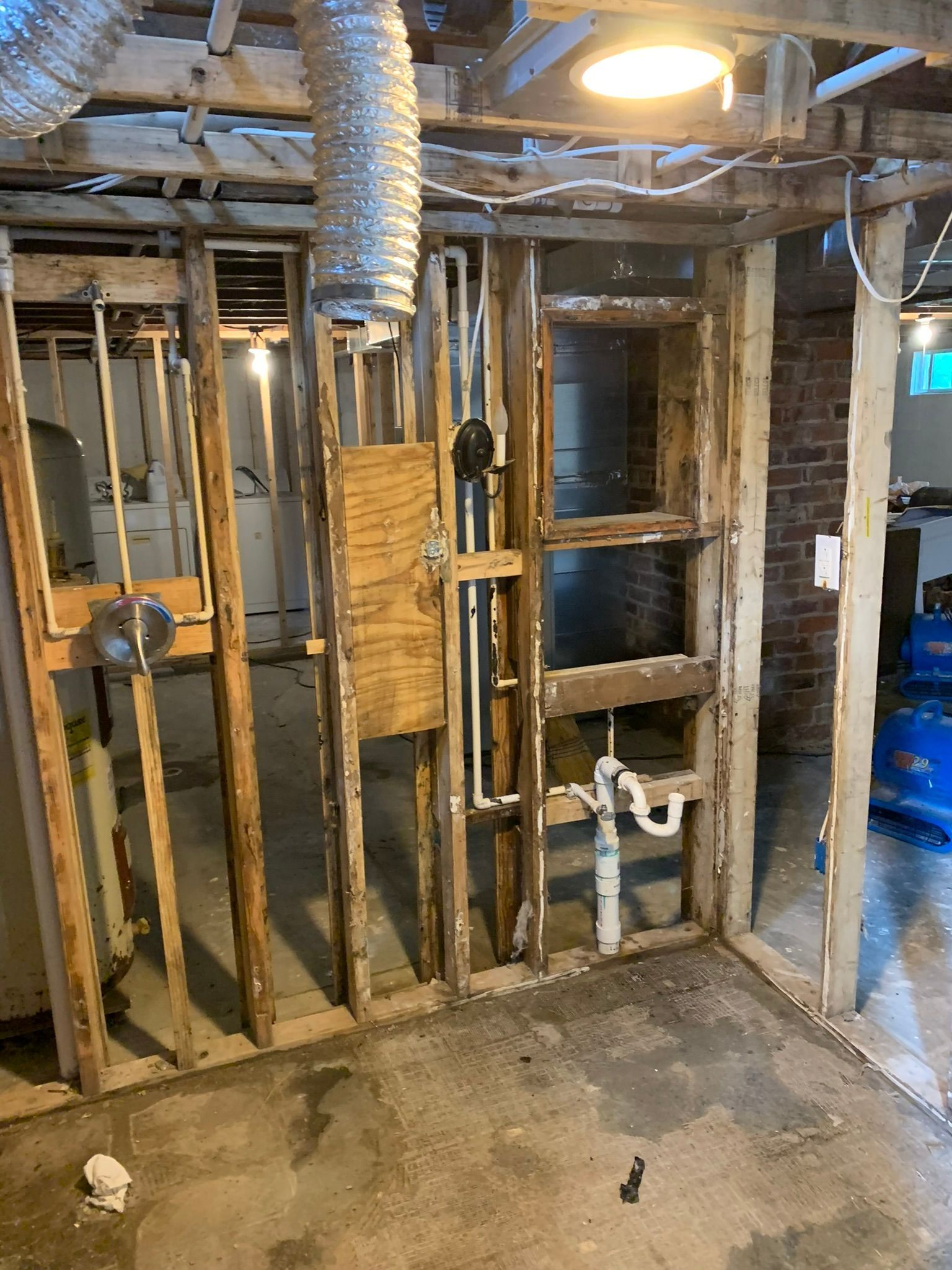 Unfinished basement wall with exposed studs, pipes, ductwork, and concrete floor.