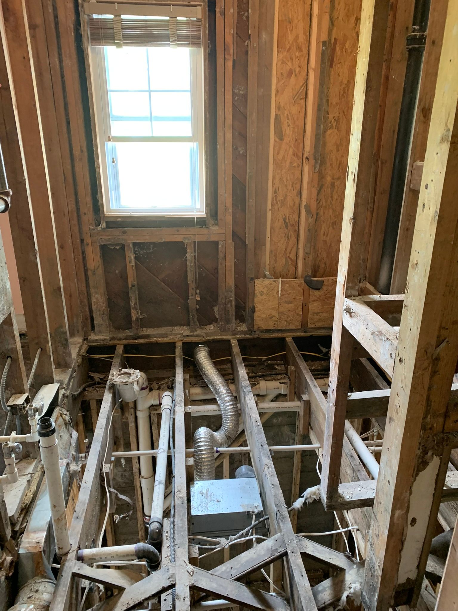 Interior of a house under renovation with exposed wall studs, floor joists, and a window.