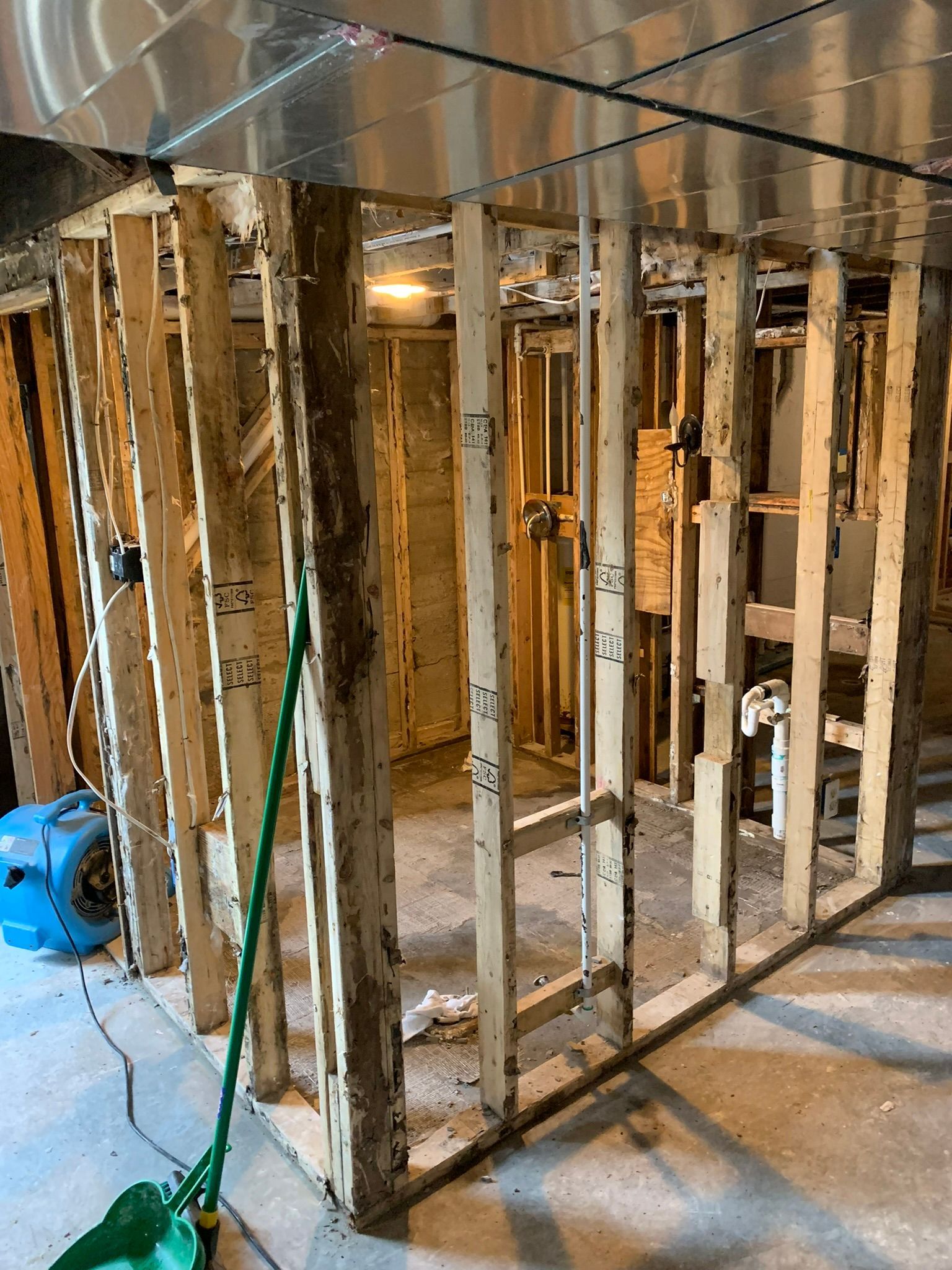 Partially framed interior room with exposed studs, tools, and debris on a concrete floor