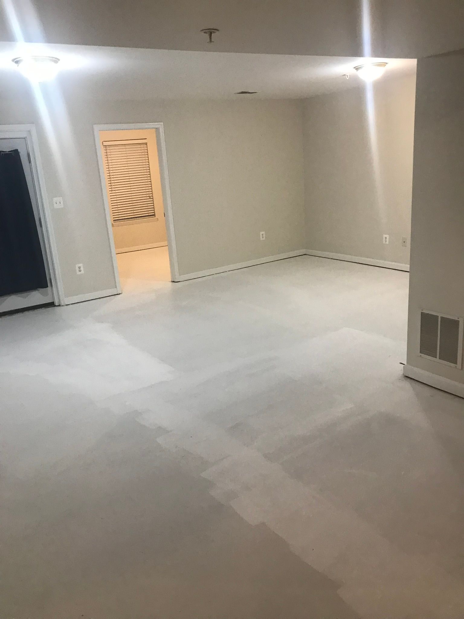 Empty beige room with white floor, recessed lights, and an open doorway to a lit hall
