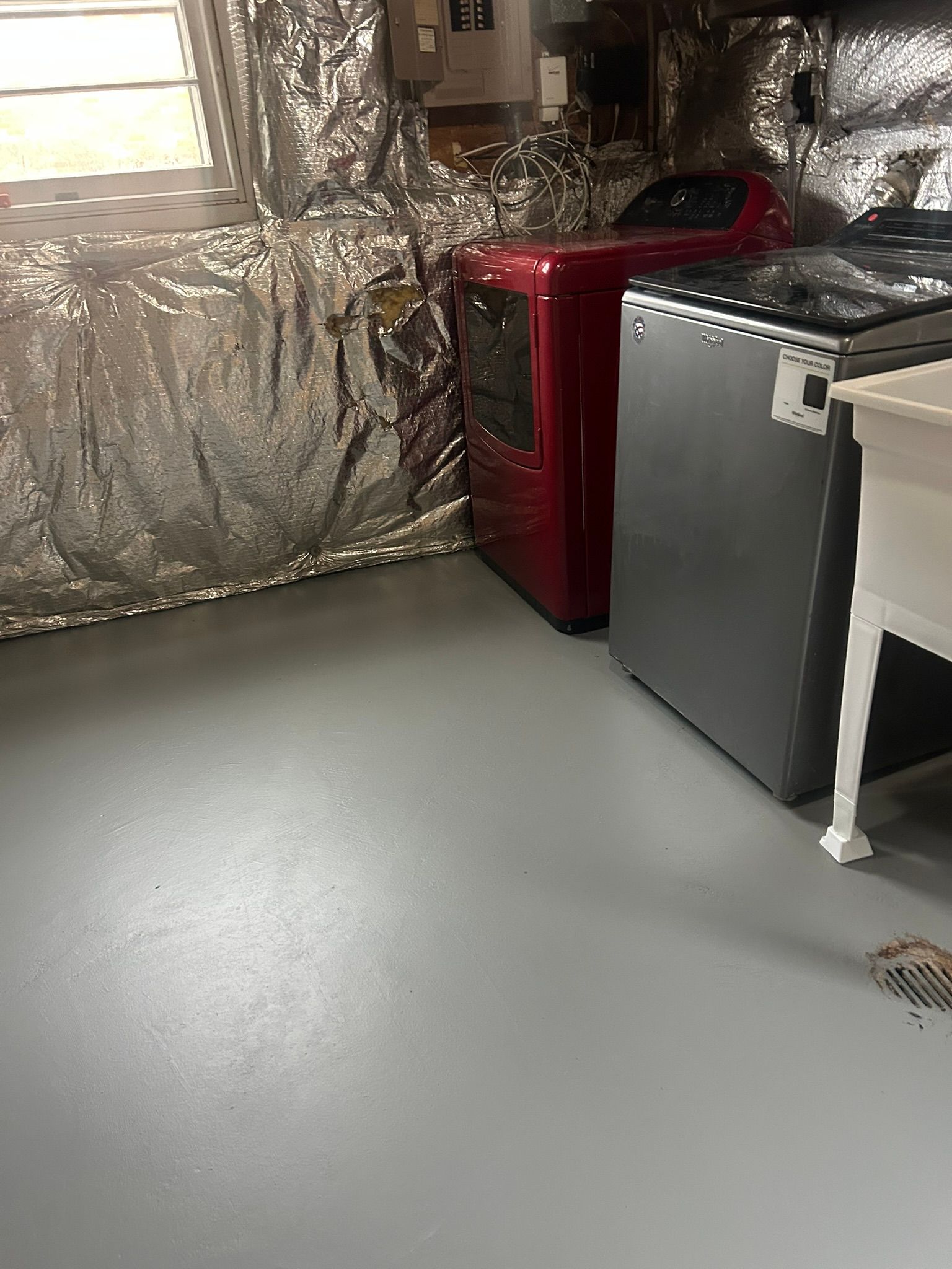 Basement room with gray floor, red appliance, silver insulation, and a workbench.