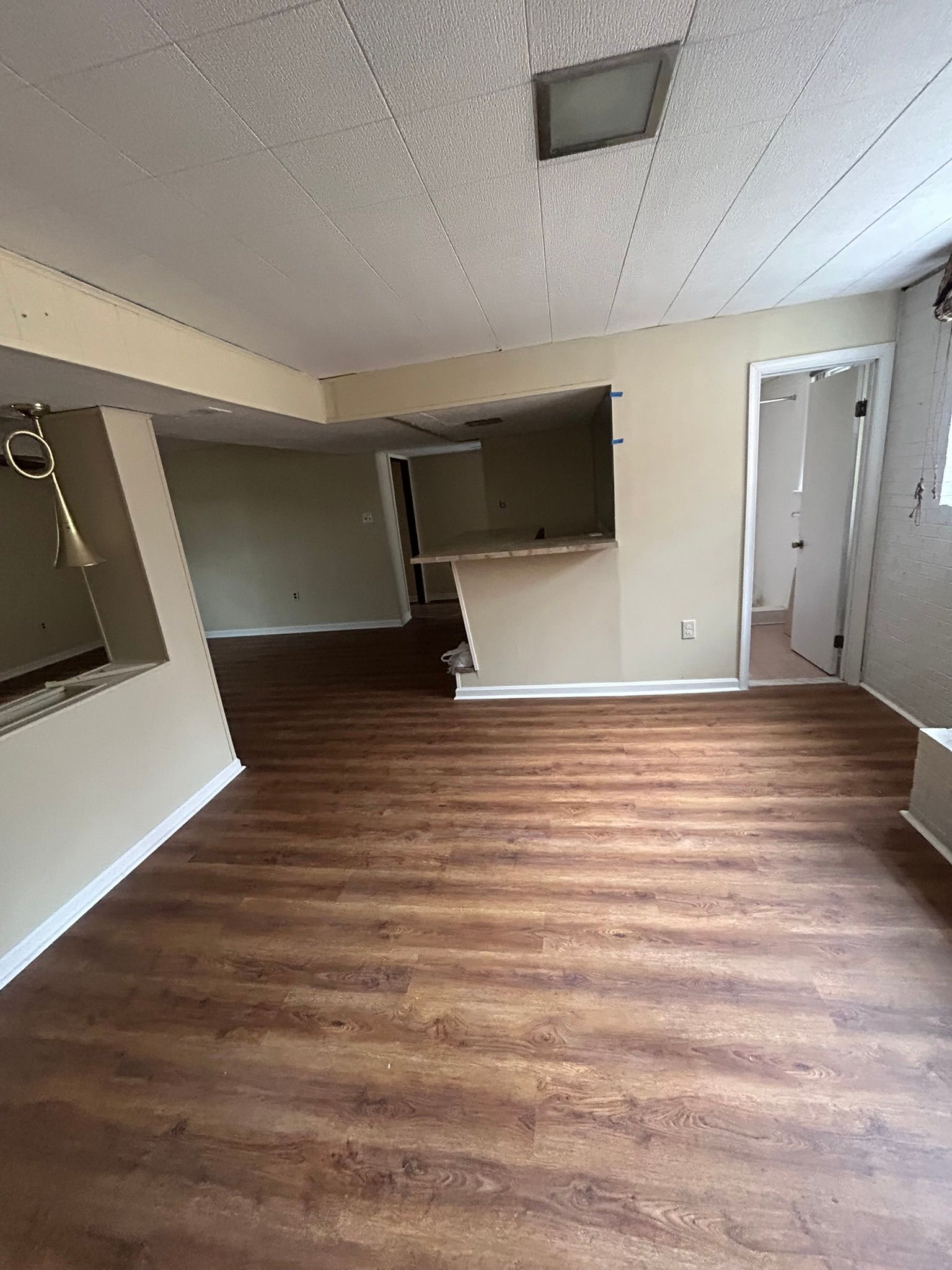 Empty room with wood floor, beige walls, and a doorway to a darker adjoining space.