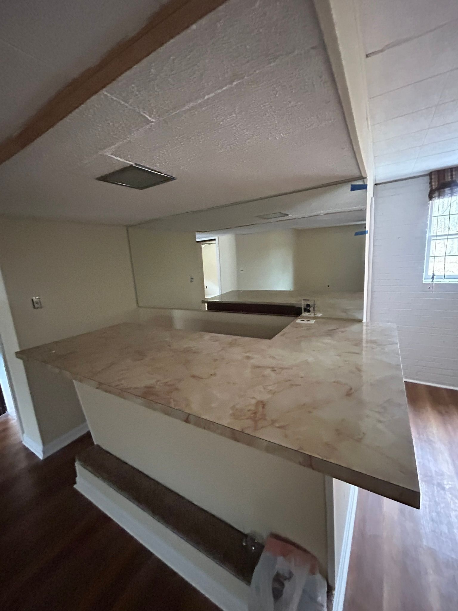 Empty unfinished kitchen with beige countertops, brown trim, and exposed ceiling tiles.