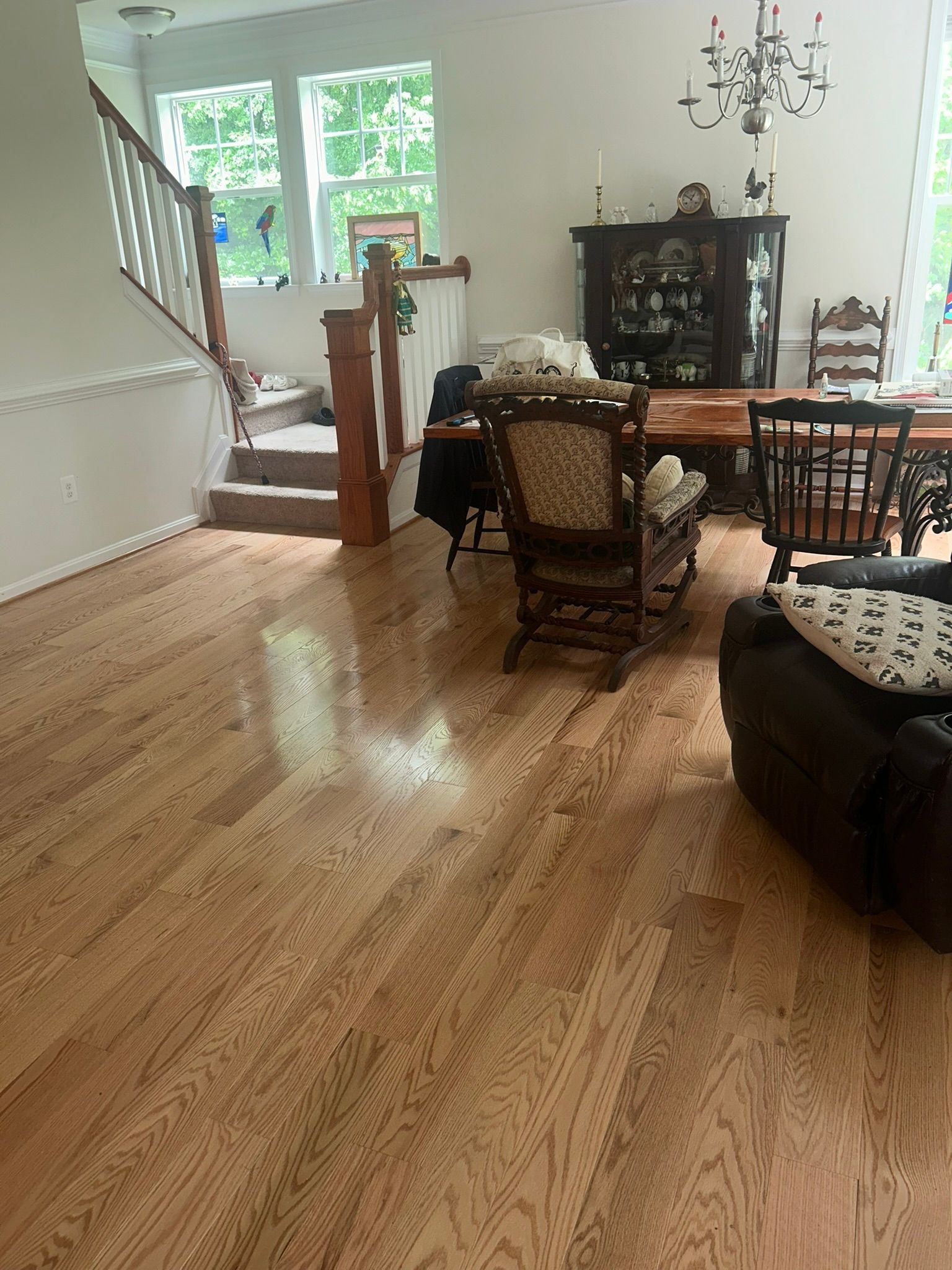 Bright living room with hardwood floors, staircase, chandelier, and dark wood furniture by large windows