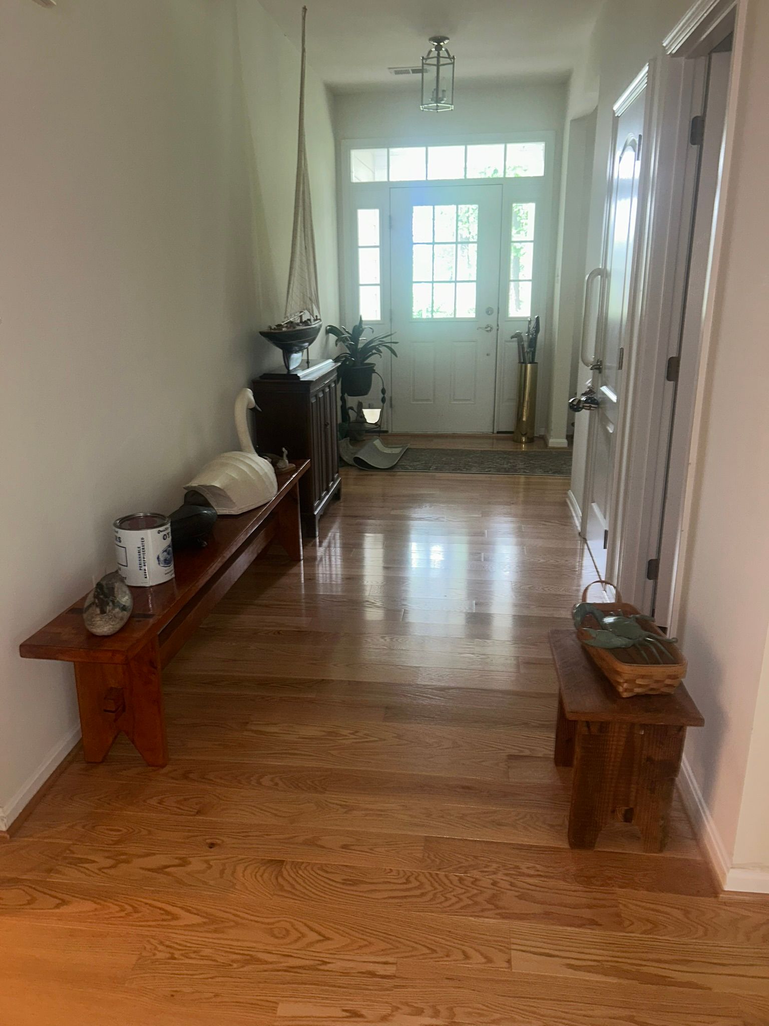 Narrow hallway with hardwood floor, benches along the walls, and a bright front door at the end.