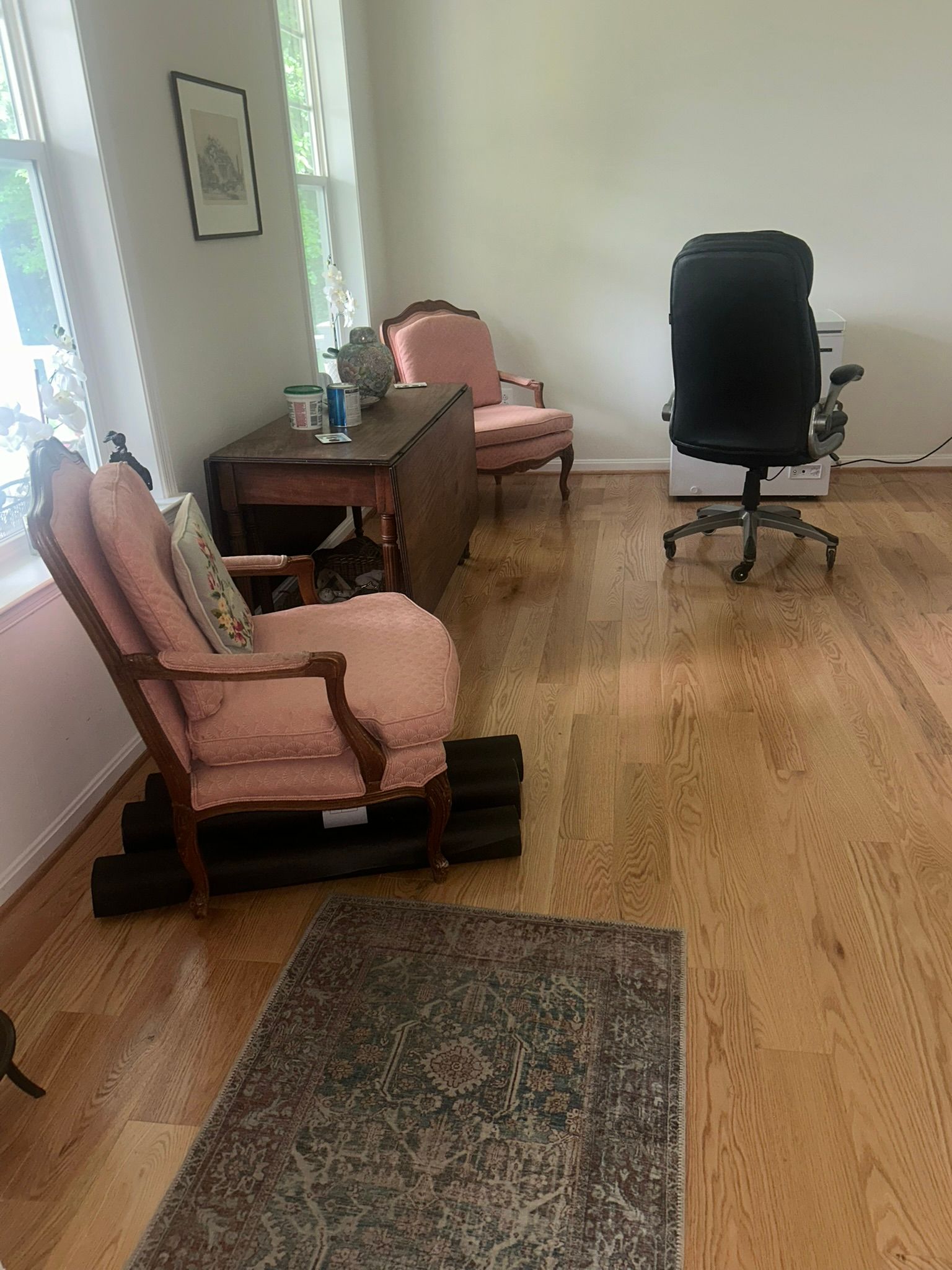 Empty living room with pink chairs, wooden table, black office chair, and a rug on hardwood floor