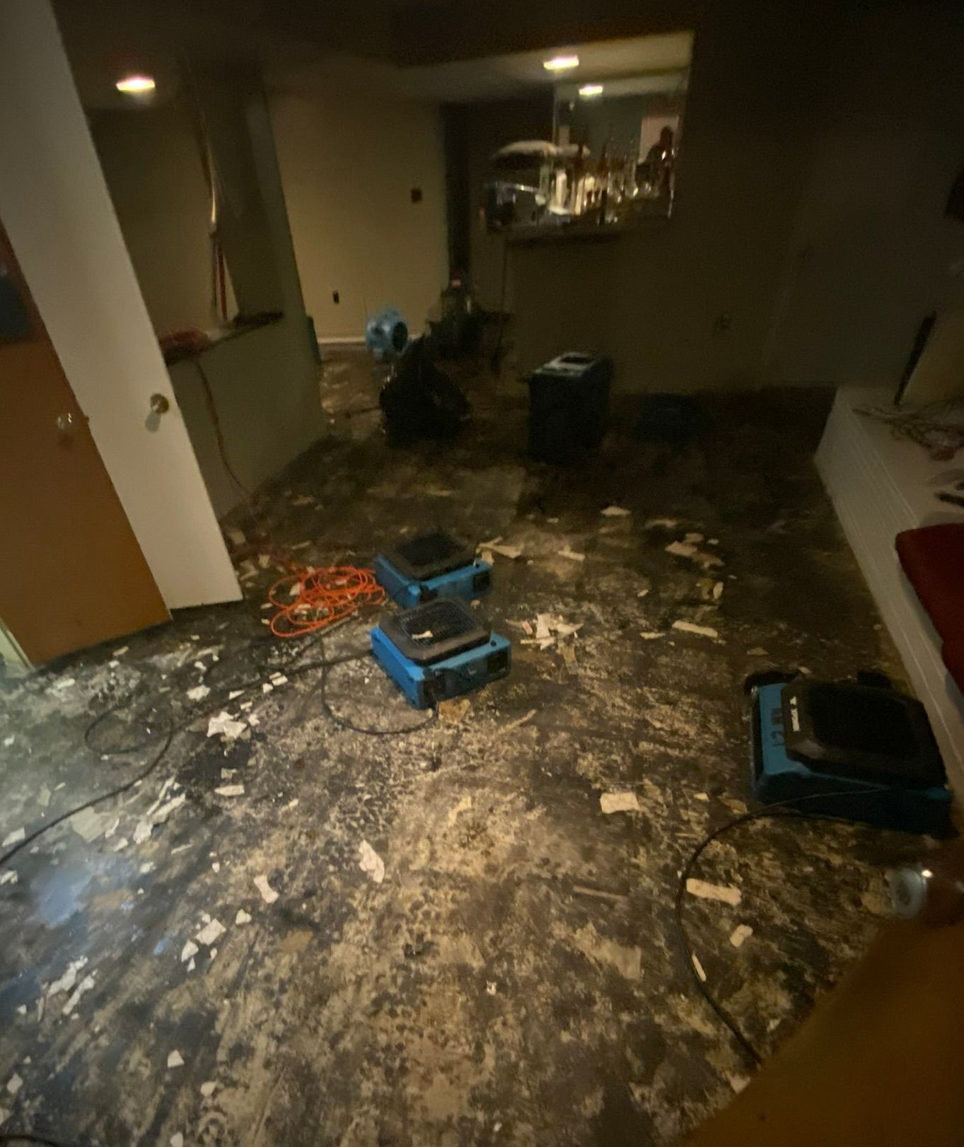 Flooded living room with muddy water, scattered debris, and a blue power tool on the floor.