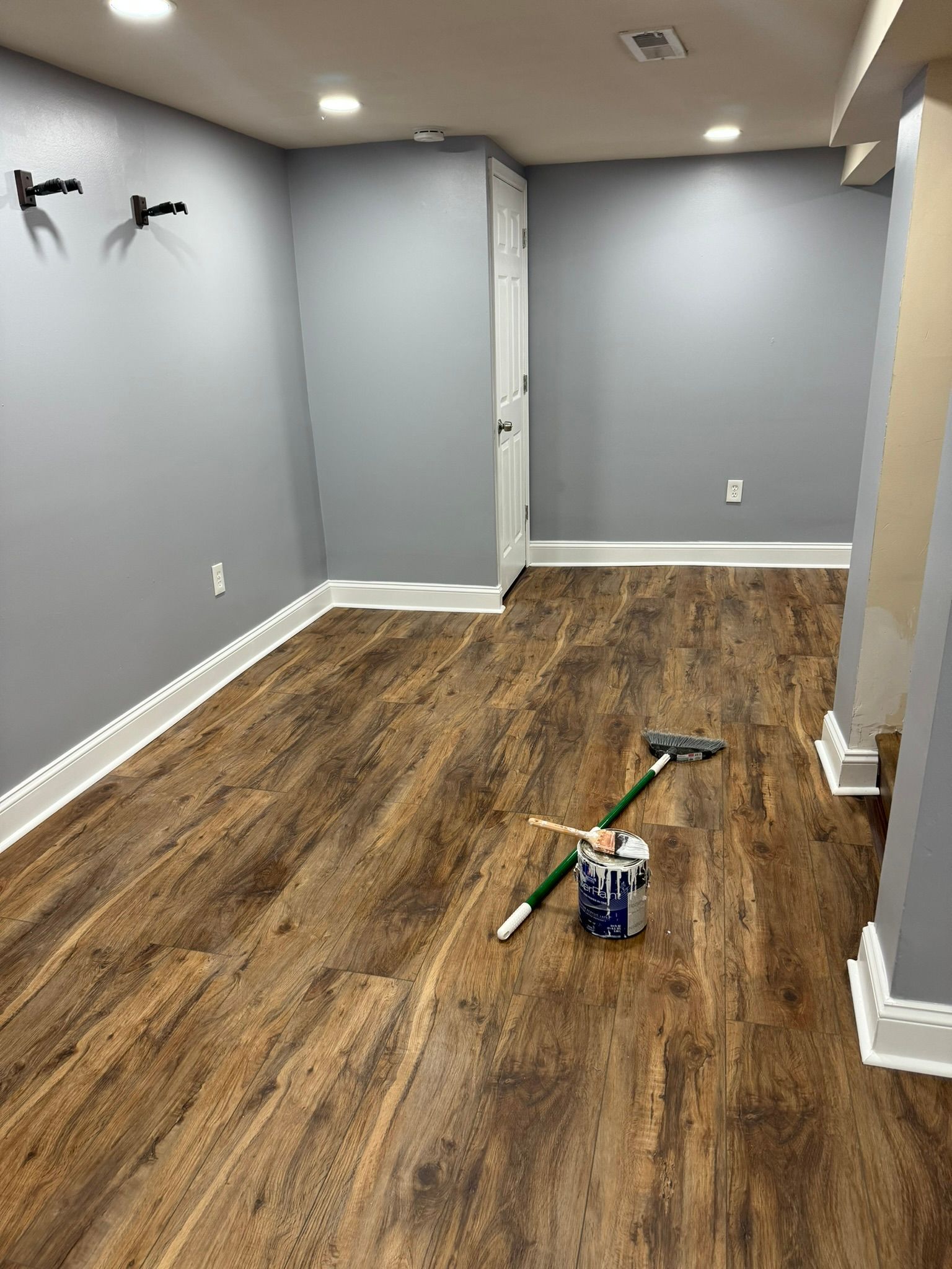 Empty gray room with wood-look flooring and cleaning tools on the floor