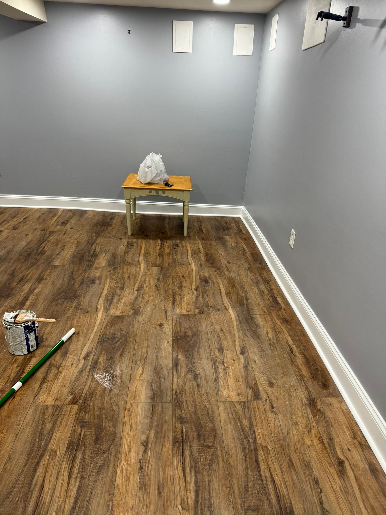 Empty gray room with wood floor, a small table at the back, and tools on the floor in the foreground