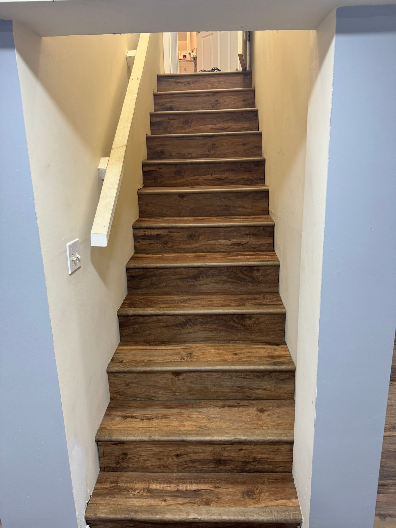 Narrow indoor staircase with brown carpeted steps and white handrails, viewed from the bottom.