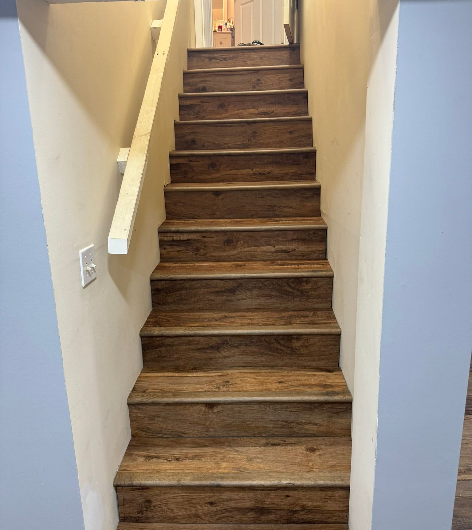 Narrow wooden staircase with beige walls and a handrail, leading up indoors