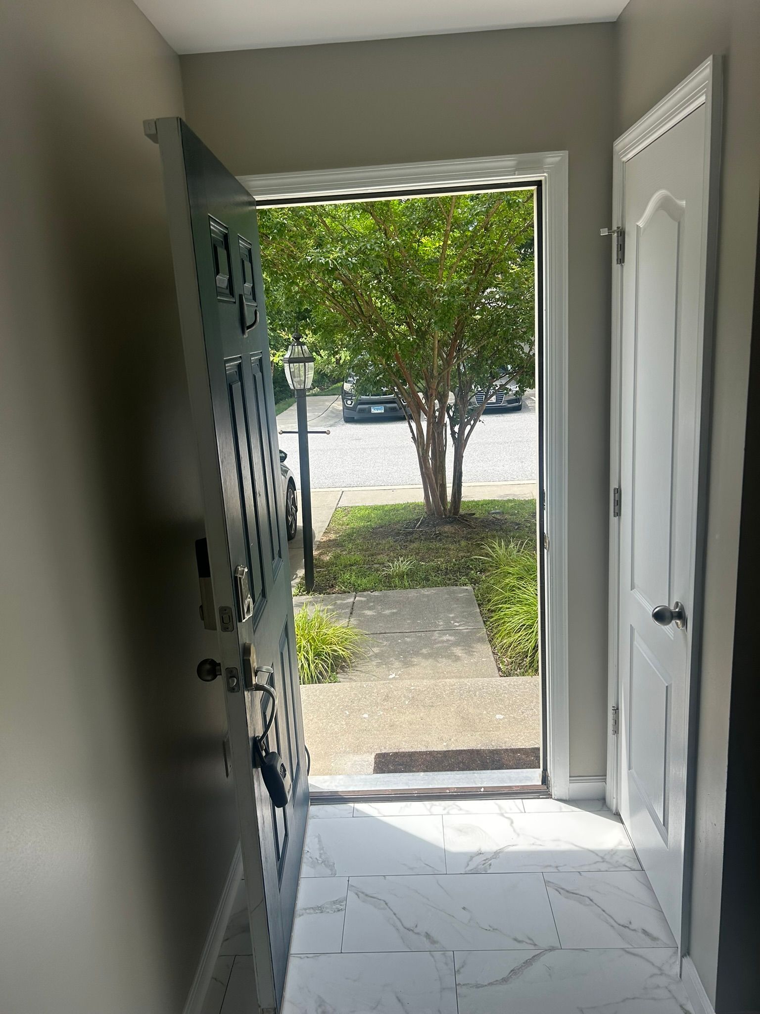 Front entry hallway opening to a sunlit walkway, tree, and street outside