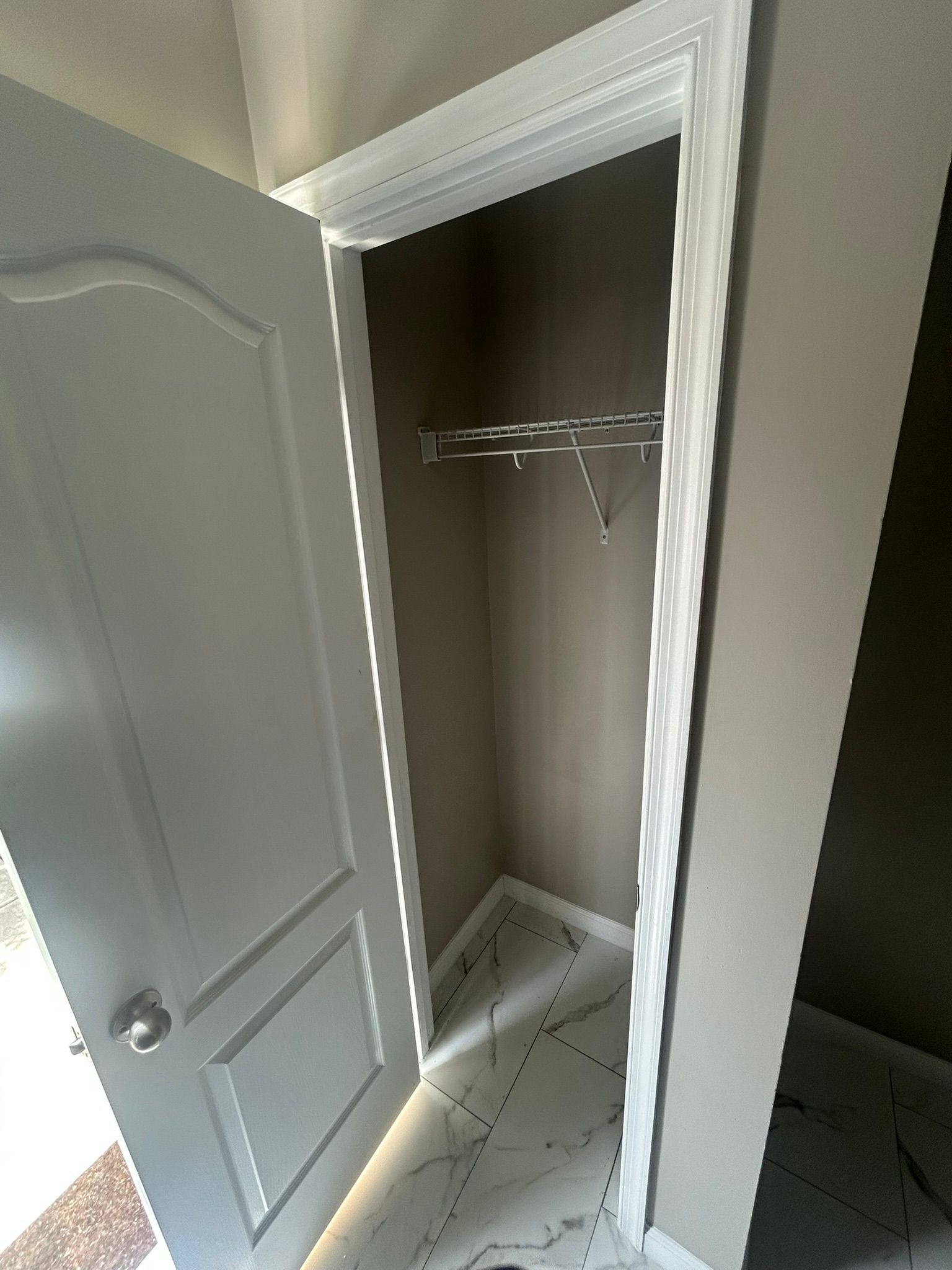 Open closet with white trim, sliding door, and wire shelf in a tiled room.