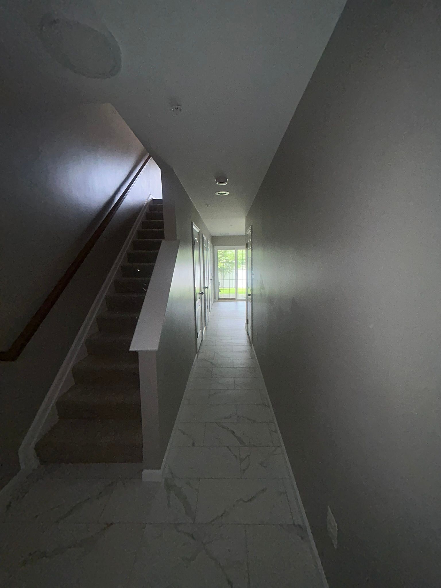 Narrow indoor stairwell with white walls, tiled floor, and bright light at the far end.