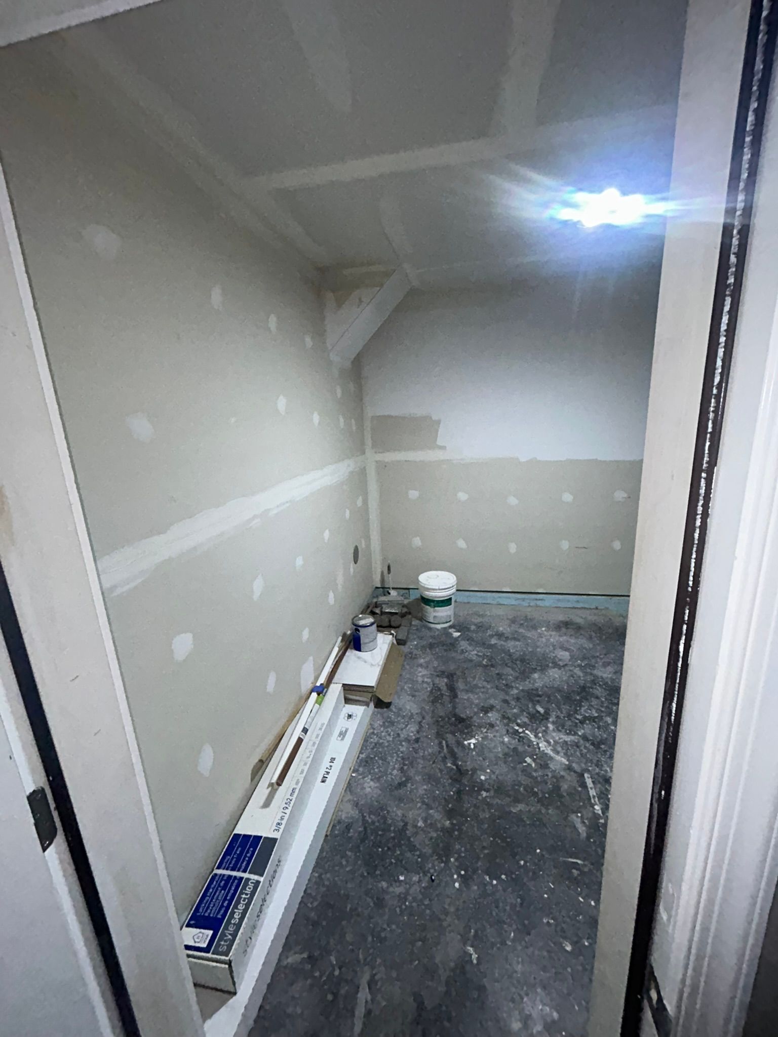 Empty unfinished room with drywall patches, construction debris, and a bucket on the floor.